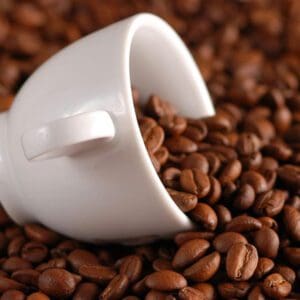 A white cup is on the ground of coffee beans.